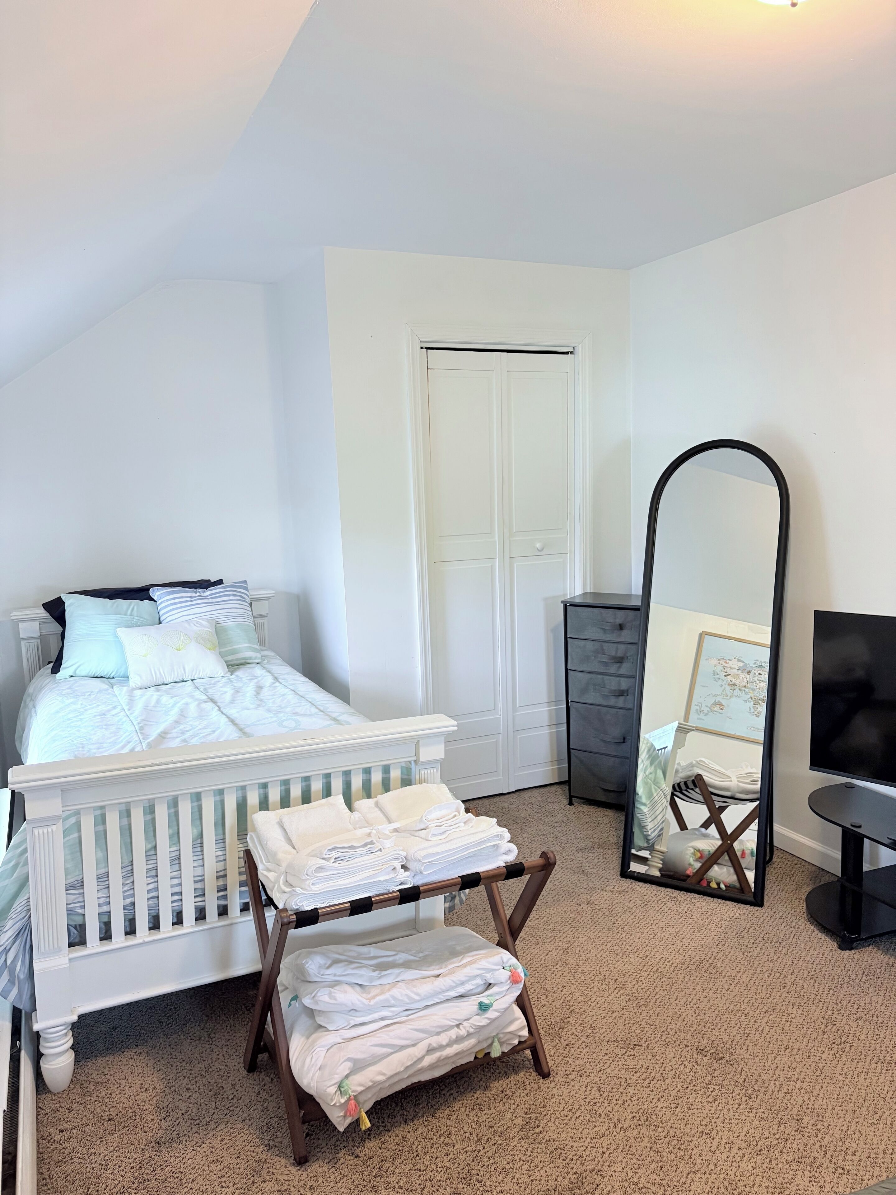 A bedroom with a white bed, a mirror, a dresser, and a TV.