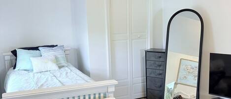 A bedroom with a white bed, a mirror, a dresser, and a TV.