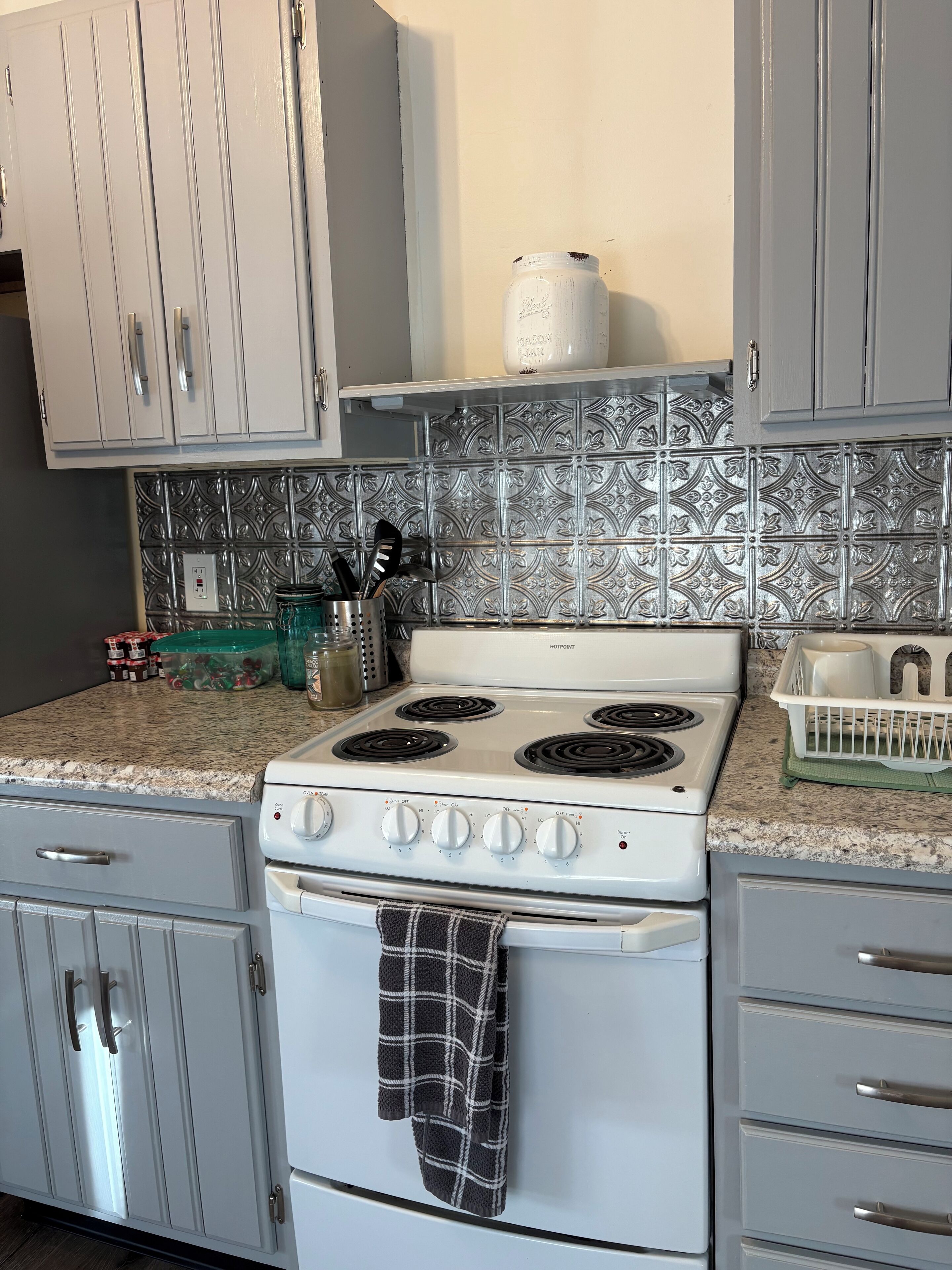 A kitchen with a white stove, grey cabinets, and a patterned backsplash.