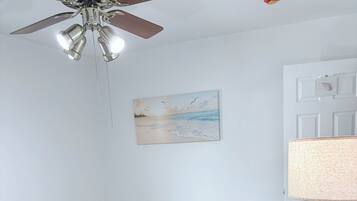 Una camera da letto con un letto, un comodino, una ventola a soffitto, un quadro e una porta.