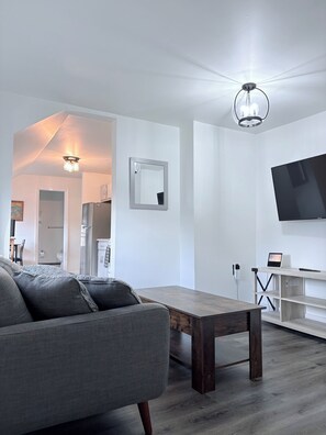 Un soggiorno moderno con un divano grigio, un tavolino in legno, una TV a schermo piatto montata a parete e una lampada a sospensione.