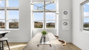 A modern dining room with a wooden table, a hanging light fixture, and large windows offering a view of the outdoors. - Tee For Two 6 Bedroom Condo (St. George)
