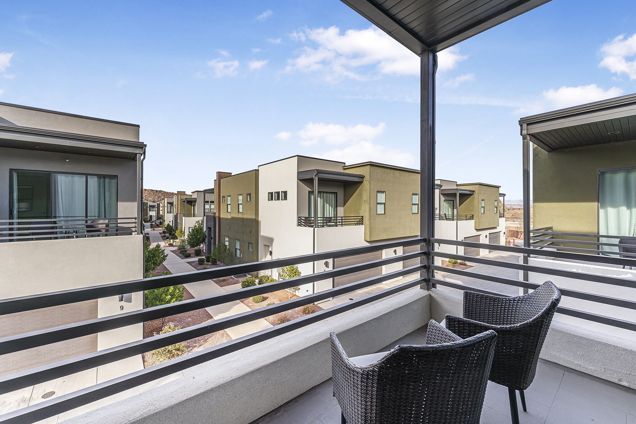 Un balcon avec des fauteuils en osier, une vue dégagée sur les bâtiments voisins et un espace extérieur bien entretenu.