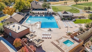 A large outdoor swimming pool with lounge chairs and umbrellas, surrounded by a landscaped area with trees and a view of distant mountains. - Tee For Two 6 Bedroom Condo (St. George)