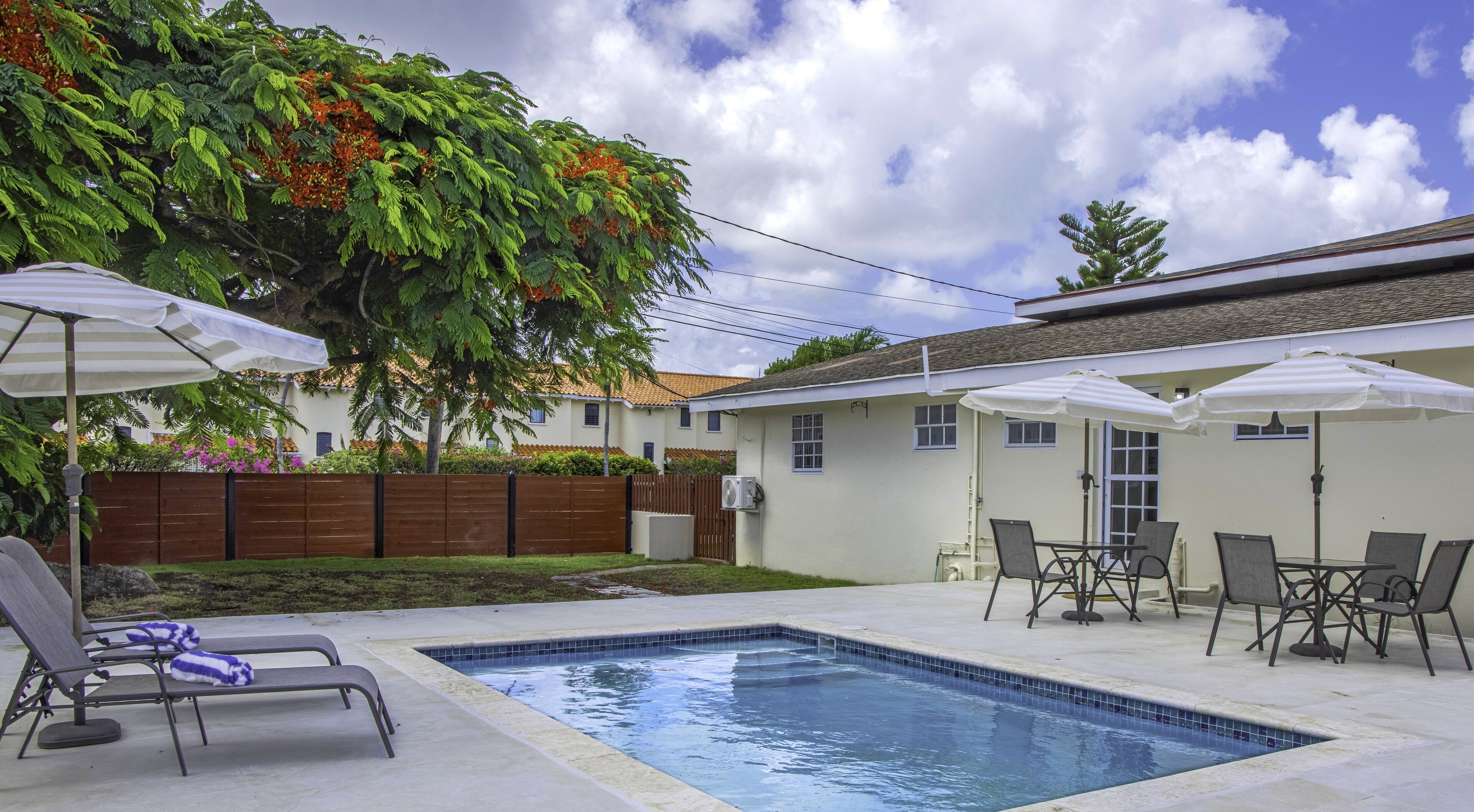 A backyard with a swimming pool, lounge chairs, and umbrellas.