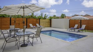 A backyard with a swimming pool, lounge chairs, and a table with an umbrella.