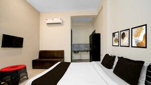 Une chambre d’hôtel avec un lit, une télévision, un petit tabouret et des œuvres d’art accrochées au mur.