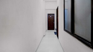 Un couloir étroit aux murs blancs, doté d’un sol carrelé, mène à une porte dont le cadre est de couleur sombre.