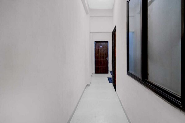 A narrow, white-walled hallway with a tiled floor leading to a door with a dark frame.