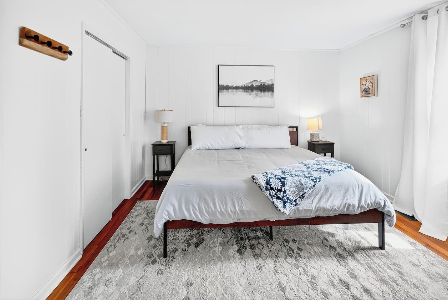 A bedroom with a bed, two bedside tables, a nightstand, a wooden bench, a rug, and a picture on the wall.