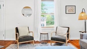 A room with two armchairs, a small round table, a floor lamp, and a large window with curtains.