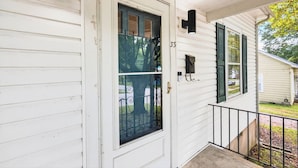A white wooden house with a front door, a small porch, and a window with a black frame.