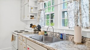A kitchen with white cabinets, a granite countertop, a stainless steel sink, and a window with floral curtains.