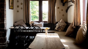 Um quarto acolhedor com uma mesa de madeira, cadeiras, um sofá e uma janela com cortinas.