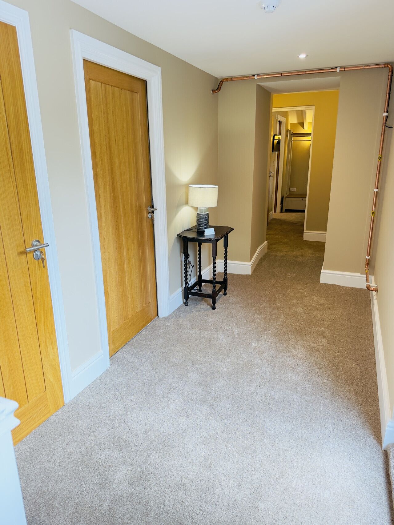 A hallway with carpeted floors, wooden doors, and a table with a lamp.