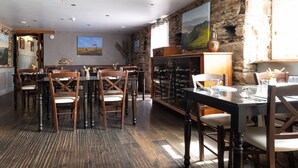 Uma área de jantar com mesas e cadeiras de madeira, uma parede de pedra e um suporte para vinhos.
