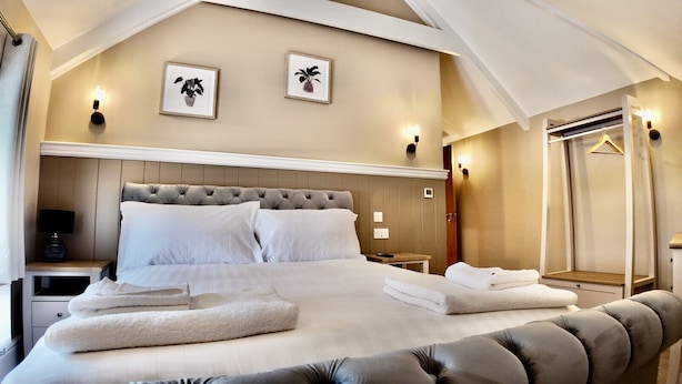 Um quarto espaçoso com uma cama grande, duas mesas de cabeceira, um criado-mudo, cabeceira de madeira e um closet amplo com espelho e cabideiro.