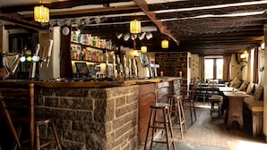 Um espaço de bar rústico com balcão de pedra, banquetas de madeira e diversos copos e garrafas.