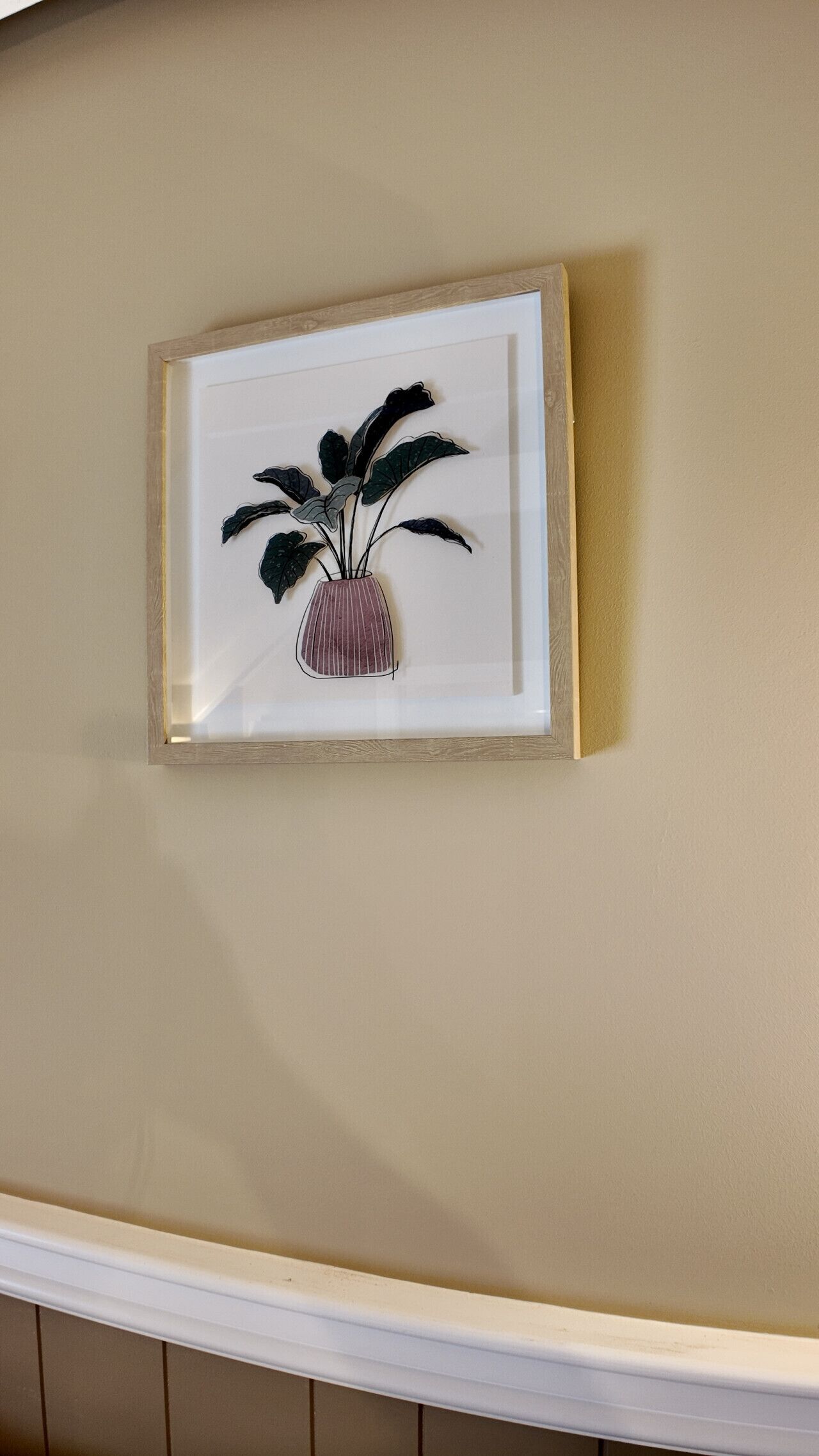 A framed artwork of a plant in a vase on a wall.