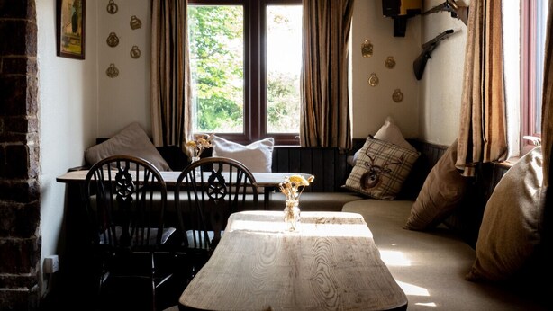 A cozy room with a wooden table, chairs, a sofa, and a window with curtains. - Rising Sun Inn - Kil Margh (Altarnun)