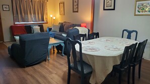 Een eetgedeelte met een ronde tafel, stoelen, een bank en een raam met gordijnen.
