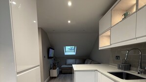 A modern kitchen with white cabinetry, a built-in island with a sink, and a small window above the island. - Modern 1-Bed Flat w/Garden|Pets & Families Welcome (Walton-on-Thames)