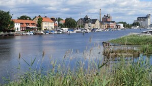 Un pueblo a orillas del río con edificios históricos, un puerto deportivo con barcos y una masa de agua tranquila.