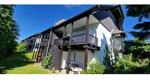 A two-story residential building with a balcony, a covered porch, and a small garden area. - Maisonette-traum mit Dachterrasse und Panorama (Willingen)