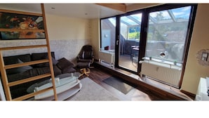 A modern living room with a glass door leading to a balcony, a sofa, a chair, and a painting on the wall. - Maisonette-traum mit Dachterrasse und Panorama (Willingen)