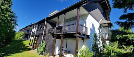 Ein zweistöckiges Wohngebäude mit Balkon, überdachter Veranda und einem kleinen Garten.