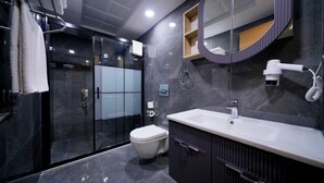 A modern bathroom with a glass-enclosed shower, a white toilet, a vanity with a mirror, and a hairdryer. - newlifecappadocia (Nevşehir)