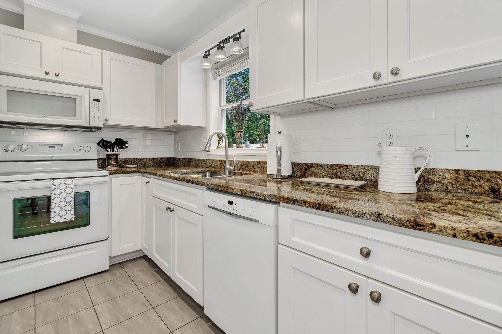 A kitchen with white cabinetry, a granite countertop, a built-in oven, a dishwasher, and a window with a view of greenery.