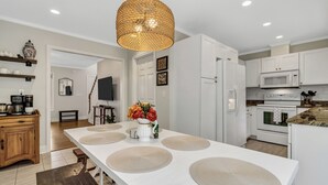 A modern kitchen with white cabinetry, a large island with placemats, a woven pendant light, and a dining area with a wooden bench. - Ridgeview Retreat with Firepit and Mountain Views (Barnardsville)