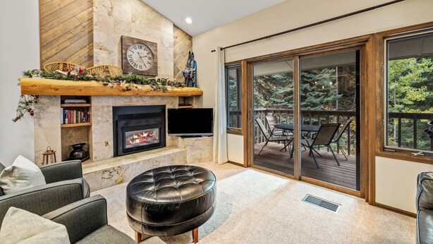 Una sala de estar moderna con chimenea, televisor y un amplio ventanal corredera que da a una terraza exterior.