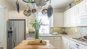 Une cuisine moderne avec des meubles blancs, un plan de travail en bois, un réfrigérateur en acier inoxydable et un porte-ustensiles suspendu.