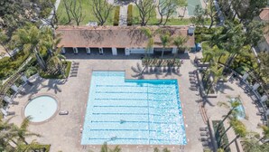 Vue aérienne d’un hôtel doté d’une grande piscine rectangulaire, de palmiers et d’un toit recouvert de tuiles.