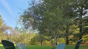 Two green Adirondack chairs facing each other with a small table in between, set on a grassy lawn with trees in the background. - Pet-friendly cottage bordering Shawnee State Forest.  Minutes from Shawnee State Park, Roosevelt Lake, Turkey Creek Lake, nature center, and hiking trails. (West Portsmouth)