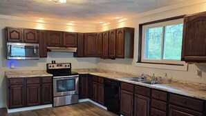 A kitchen with dark wood cabinets, stainless steel appliances, and a window with a view of trees. - Pet-friendly cottage bordering Shawnee State Forest.  Minutes from Shawnee State Park, Roosevelt Lake, Turkey Creek Lake, nature center, and hiking trails. (West Portsmouth)