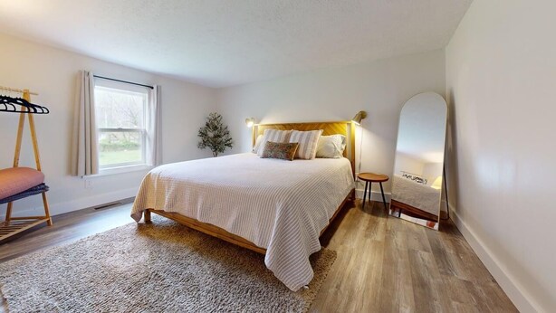 A bedroom with a bed, a bedside table, a mirror, a window, and a hanging chair. - Pet-friendly cottage bordering Shawnee State Forest.  Minutes from Shawnee State Park, Roosevelt Lake, Turkey Creek Lake, nature center, and hiking trails. (West Portsmouth)