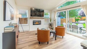 Una sala de estar moderna con chimenea, dos sillones, una mesa de centro y vistas al jardín trasero a través de amplios ventanales correderos.