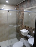 Un baño moderno con cabina de ducha de vidrio, inodoro blanco y encimera de granito con lavamanos.