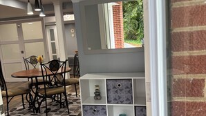 A modern kitchen with a wooden dining table and chairs, a built-in white shelving unit with decorative items, and a view of a brick wall and greenery outside. - Quiet 2BR Retreat Near Downtown Albemarle (Albemarle)