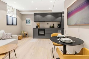 A compact living space with a kitchenette, a dining area with yellow chairs, a sofa, and a painting on the wall.