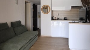 Un salon avec un canapé, un coin cuisine doté de meubles blancs et un escalier menant à l’étage supérieur.