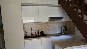 Une cuisine de taille réduite avec des meubles blancs, un évier en acier inoxydable et une machine à café.