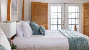 Ein Schlafzimmer mit einem großen Bett, Holzklappläden, einem gerahmten Bild und einem Topf mit einer Pflanze.