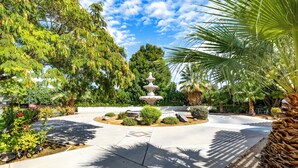 Ein angelegter Garten mit einem zentralen Brunnen, umgeben von verschiedenen Pflanzen und Bäumen.