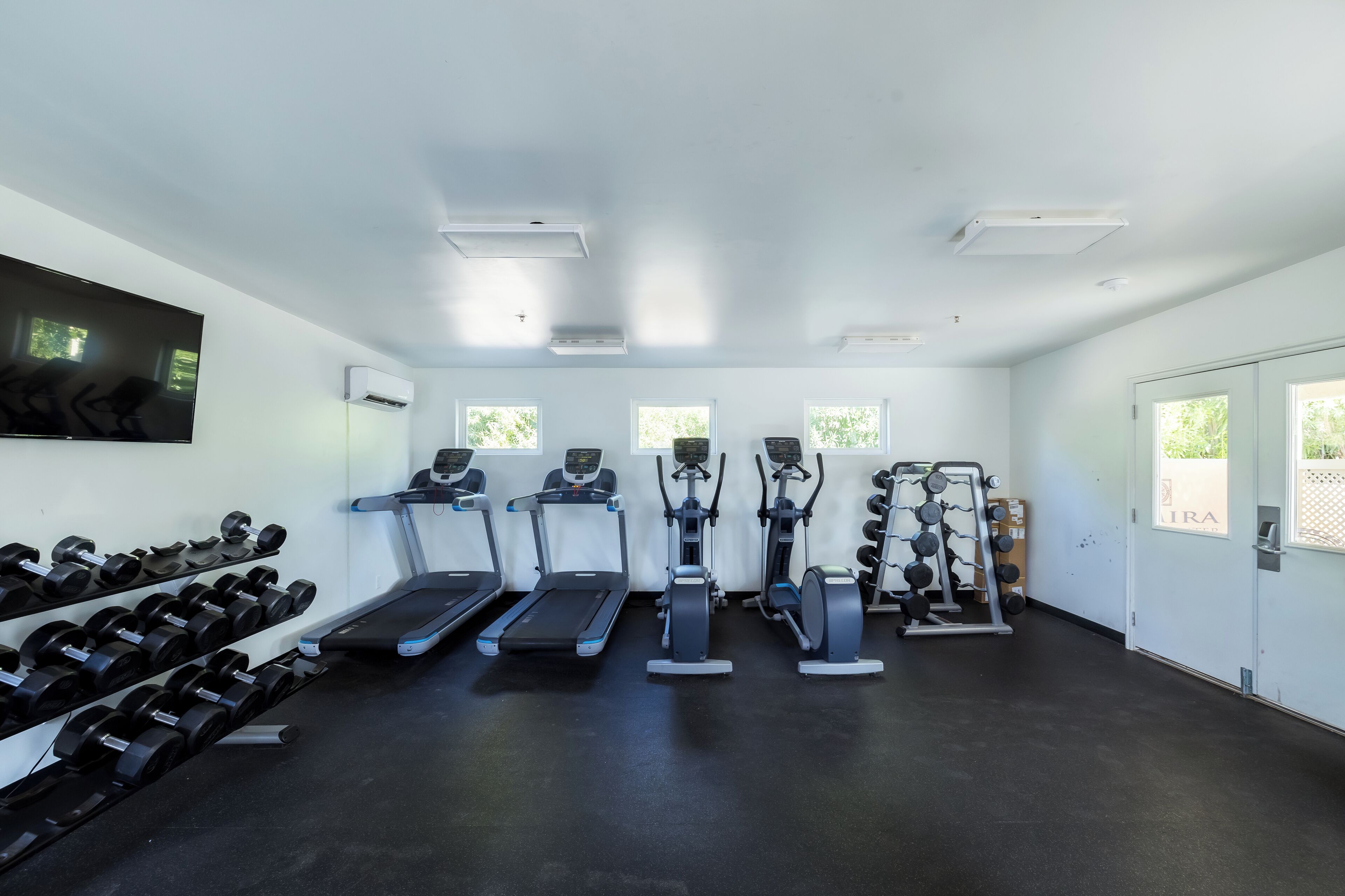 A gym with treadmills, elliptical machines, and a weight rack.