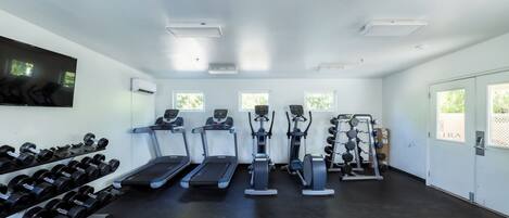 A gym with treadmills, elliptical machines, and a weight rack.