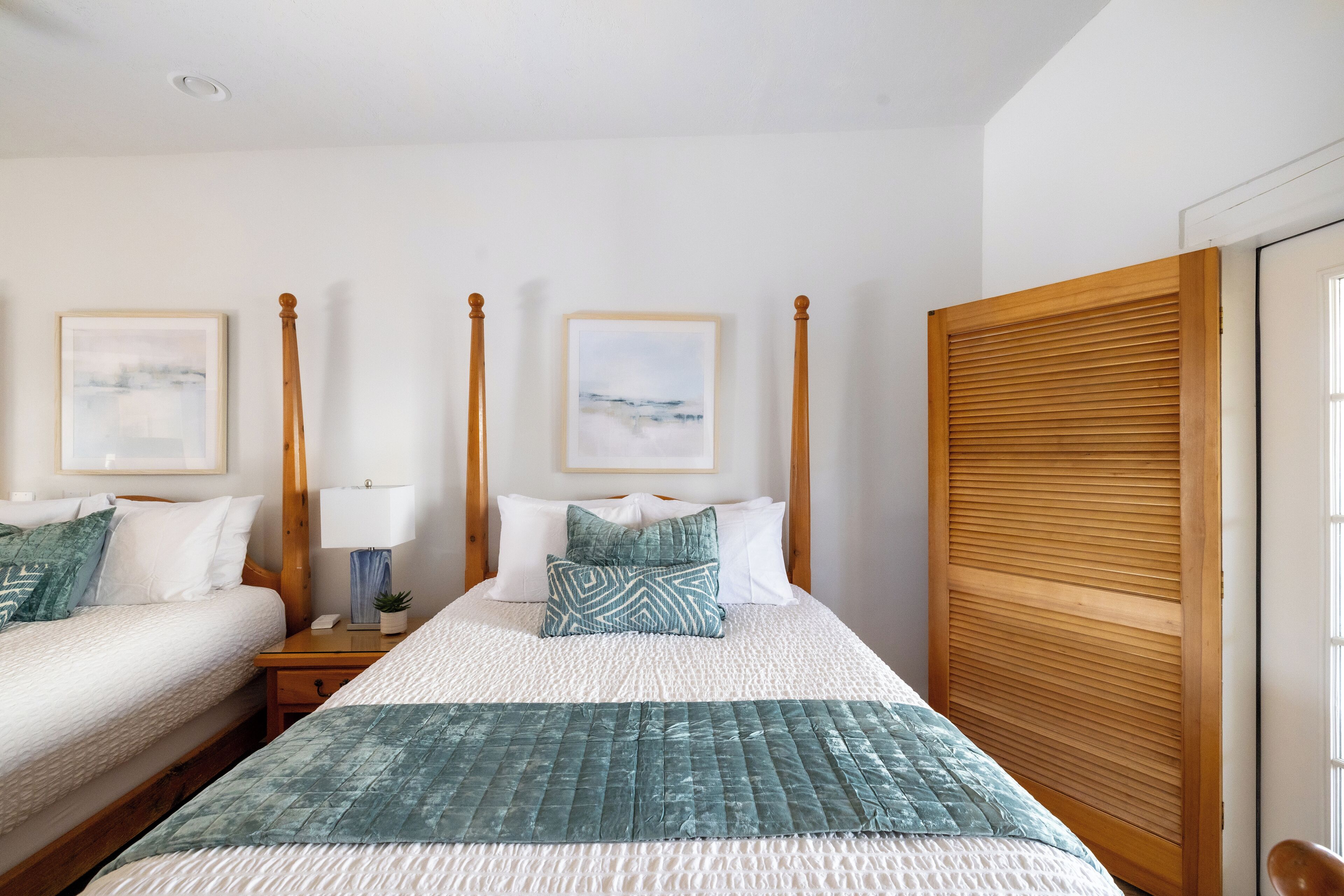 A hotel room with two beds, wooden headboards, a large window, and artwork on the walls.